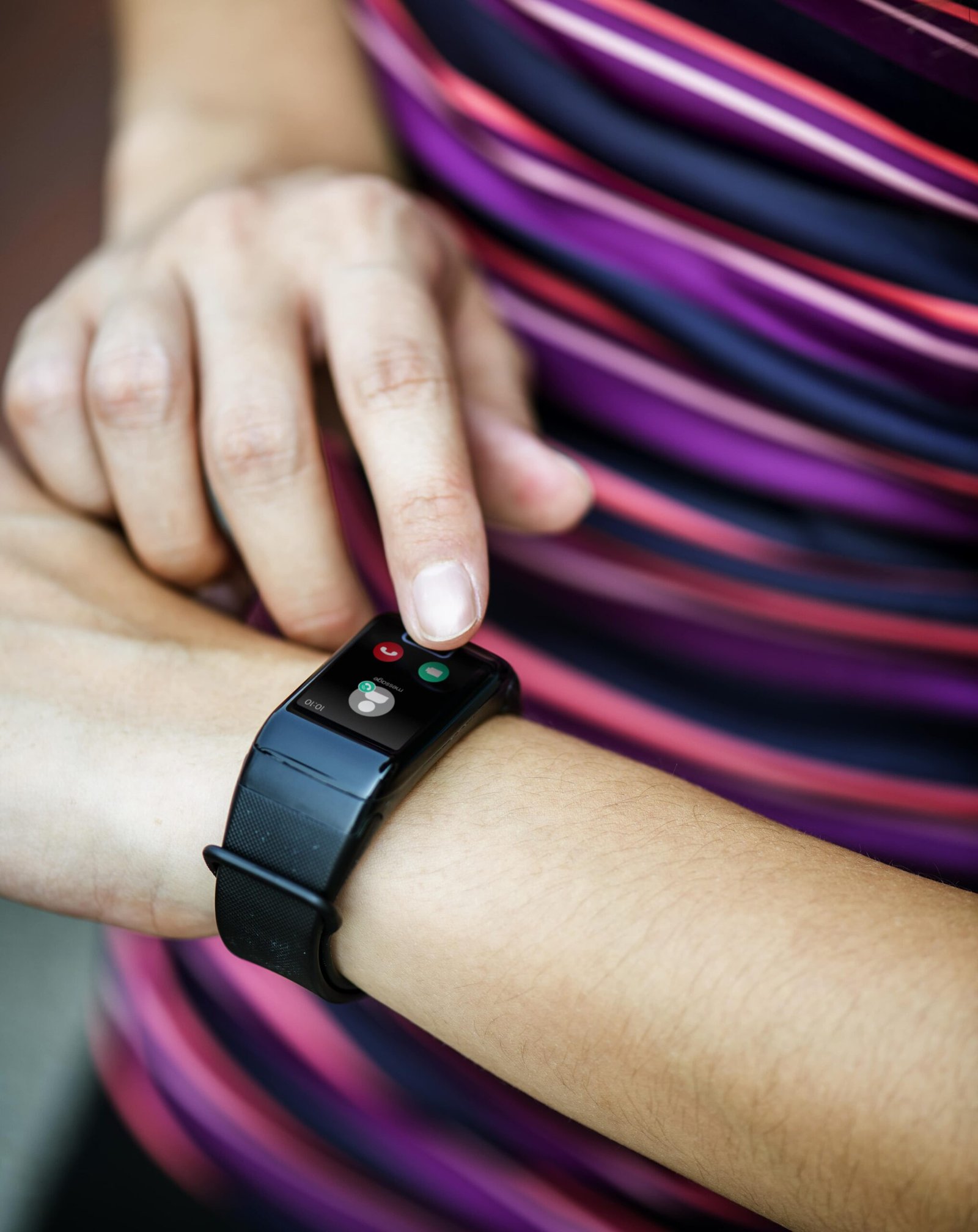 A person wearing a Fitbit Charge 6, interacting with the device's touchscreen. The fitness tracker displays call notifications, highlighting its smart functionality. The individual is dressed in a colorful, striped top, suggesting an active lifestyle.