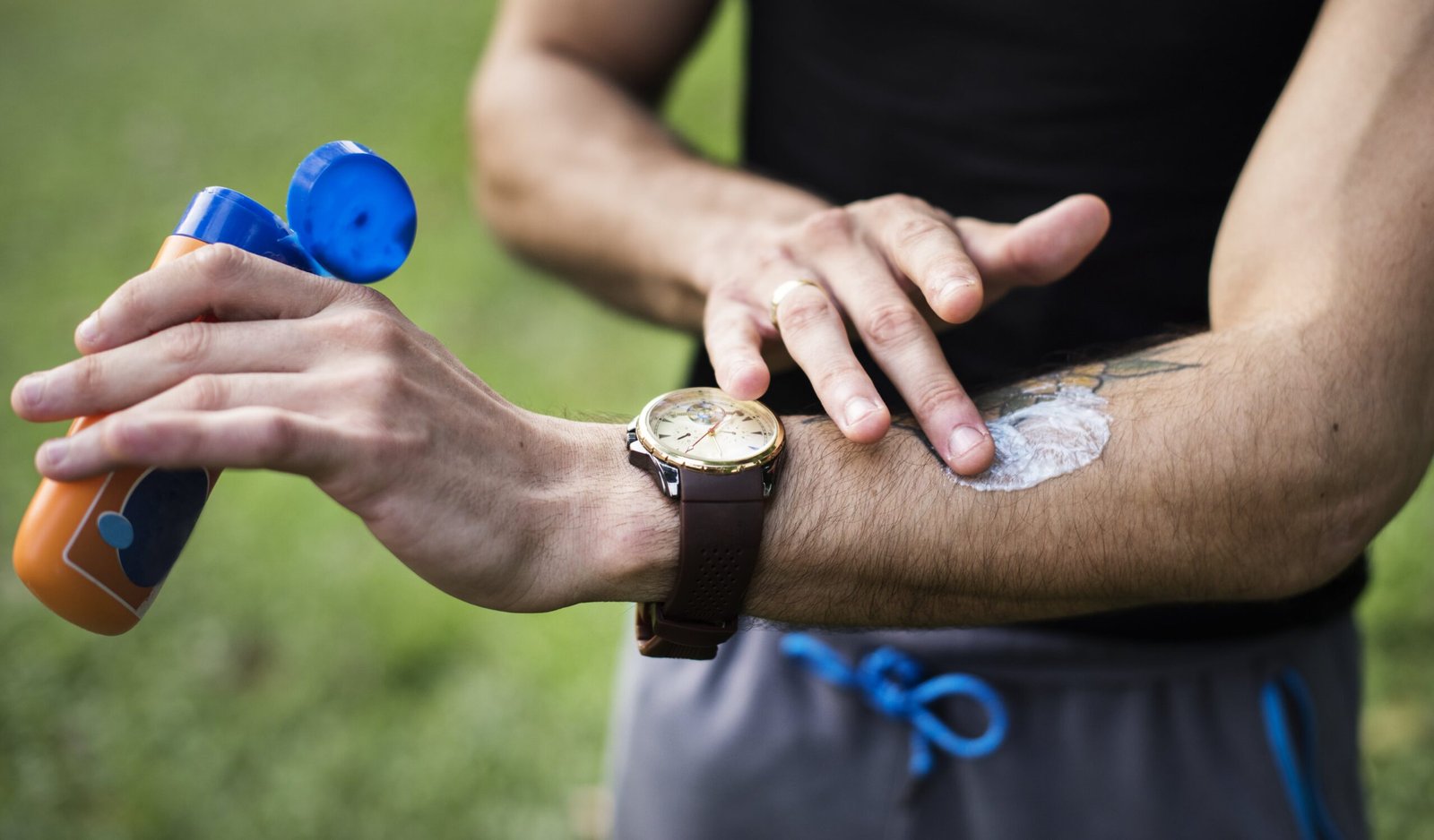 "Man applying sunscreen on his arm while wearing a wristwatch, preparing for outdoor activity